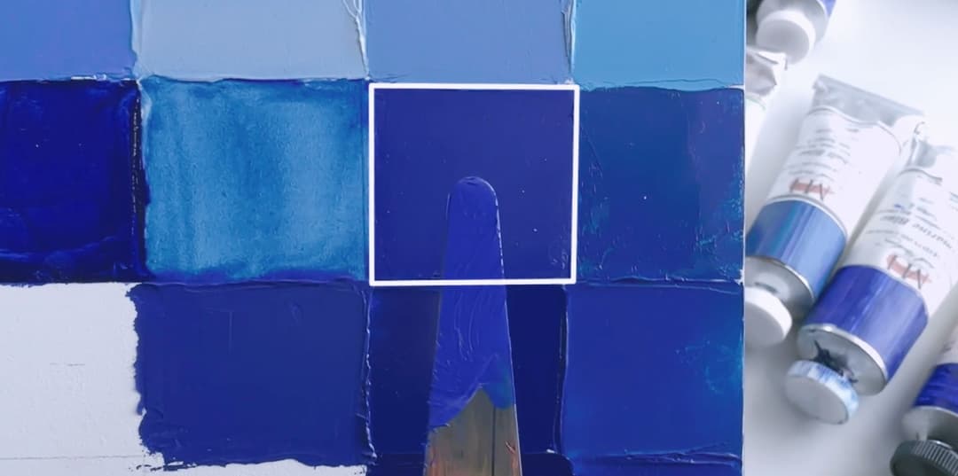 A palette knife with paint is held up against a panel with YInMn blue. The mix is close but the palette knife mix looks a bit more chromatic than the target.