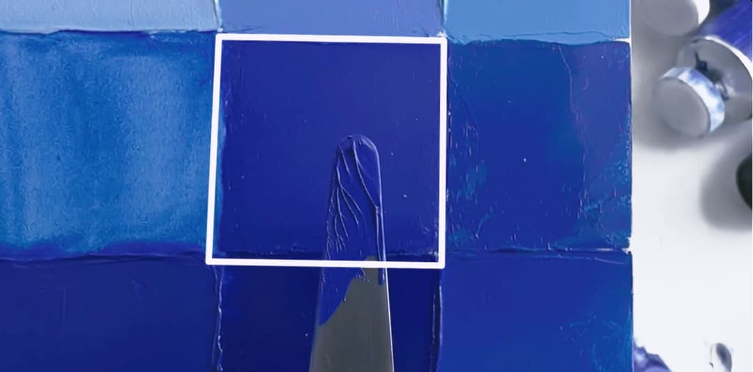 A mix of paint on a palette knife held up for comparison with the background panel.