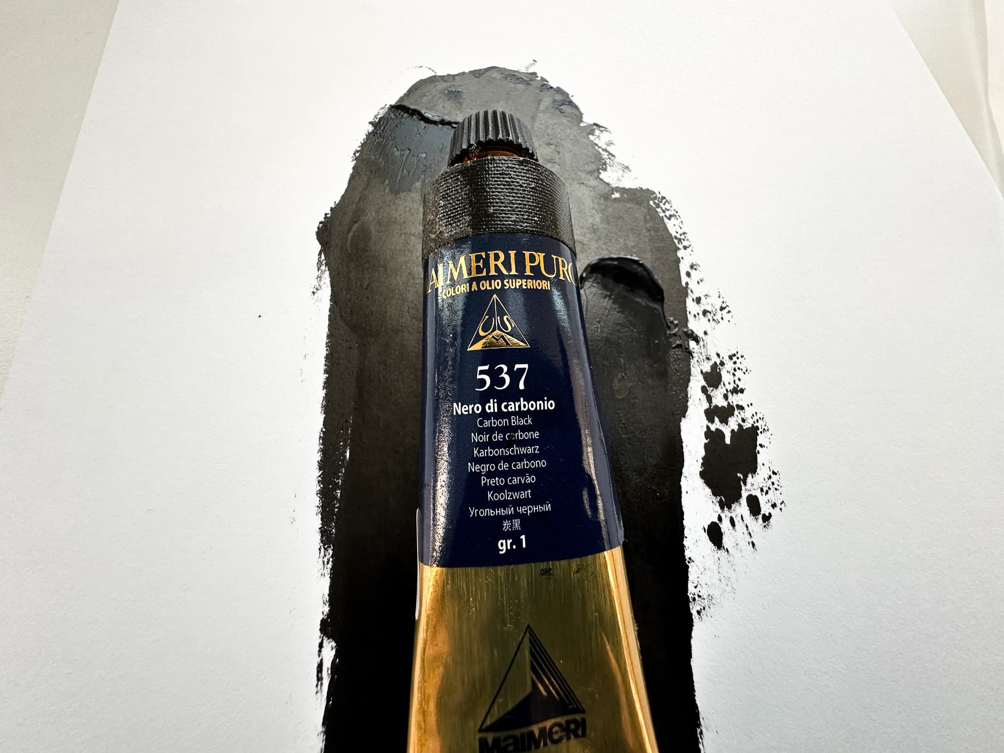 A tube of Maimeri Puro Carbon Black with a coat of oil paint in the background
