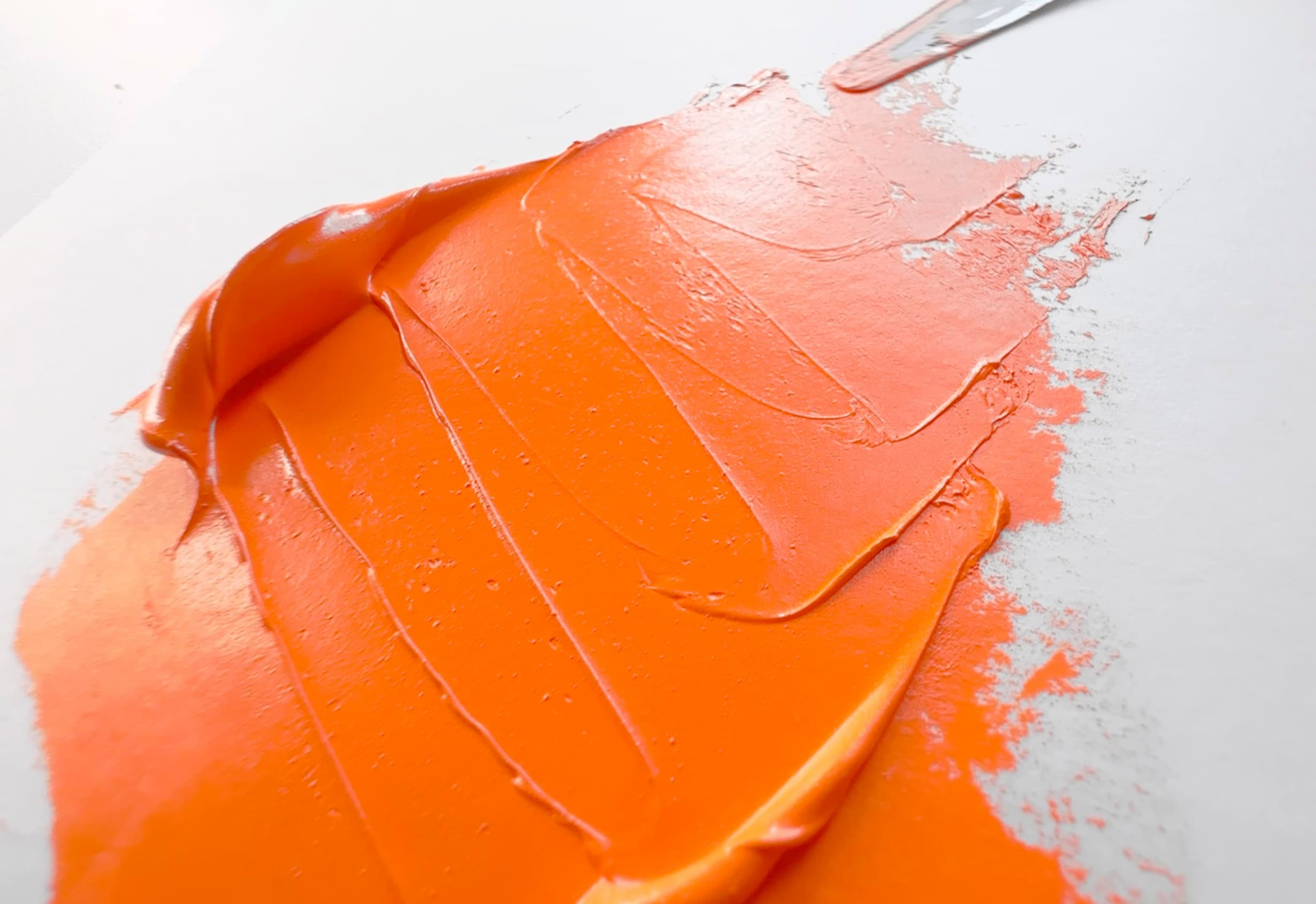 A dollop of bright orange oil paint in a swish made by a palette knife