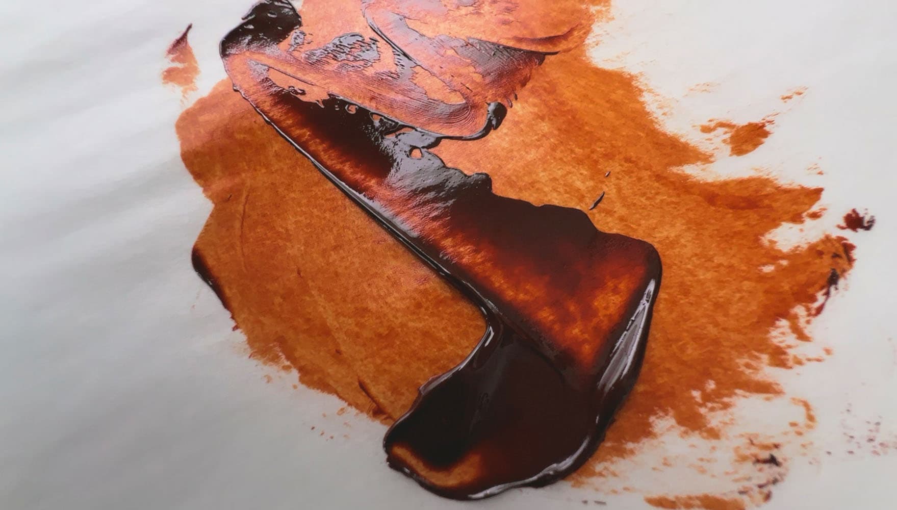 A stroke of brown oil paint which is a vibrant orange when thinned